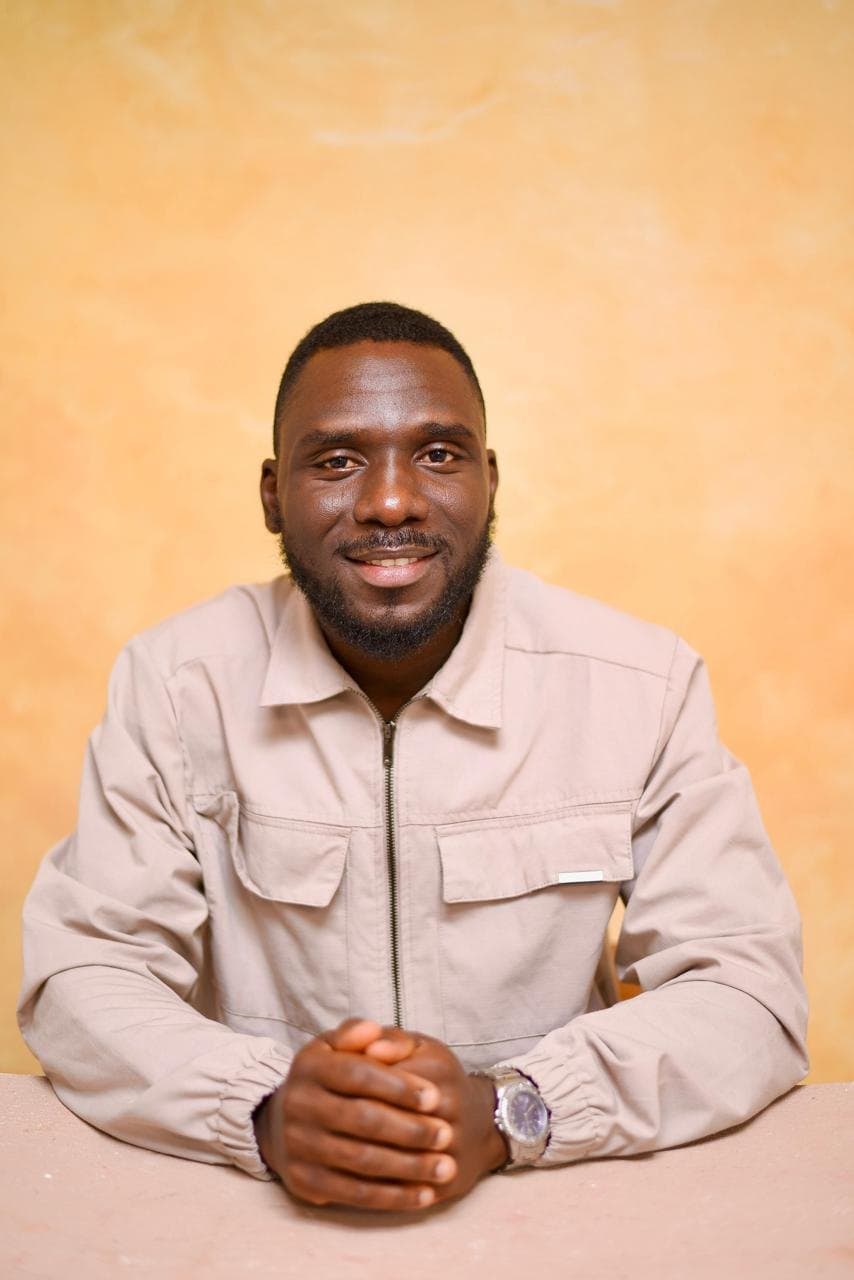 Oyewale seated at a table, hands folded, smiling